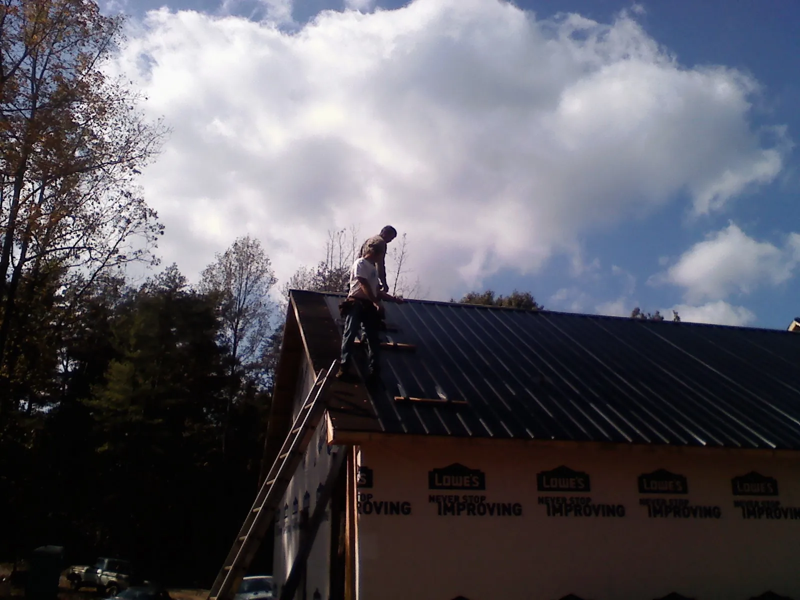 Roofer fastening dark metal panels high against a cloudy sky, from a Roof Inspection job in Pomeroy